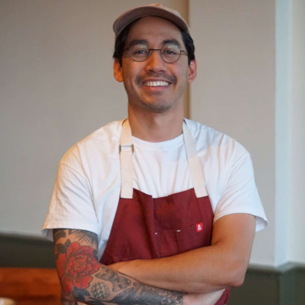 Elijah-Deleon smiling with his arms crossed in a red apron