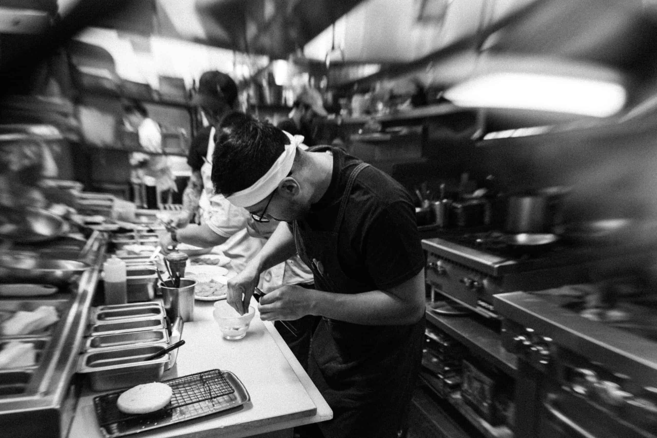 black and white photo of cooks plating dishes in the kitchen